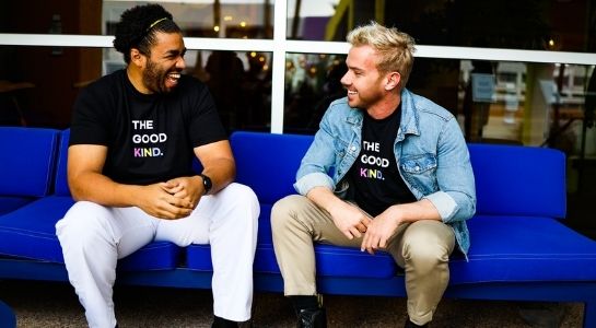 photo of two humans wearing only human shirts that read "The Good Kind" while smiling at one another on a couch