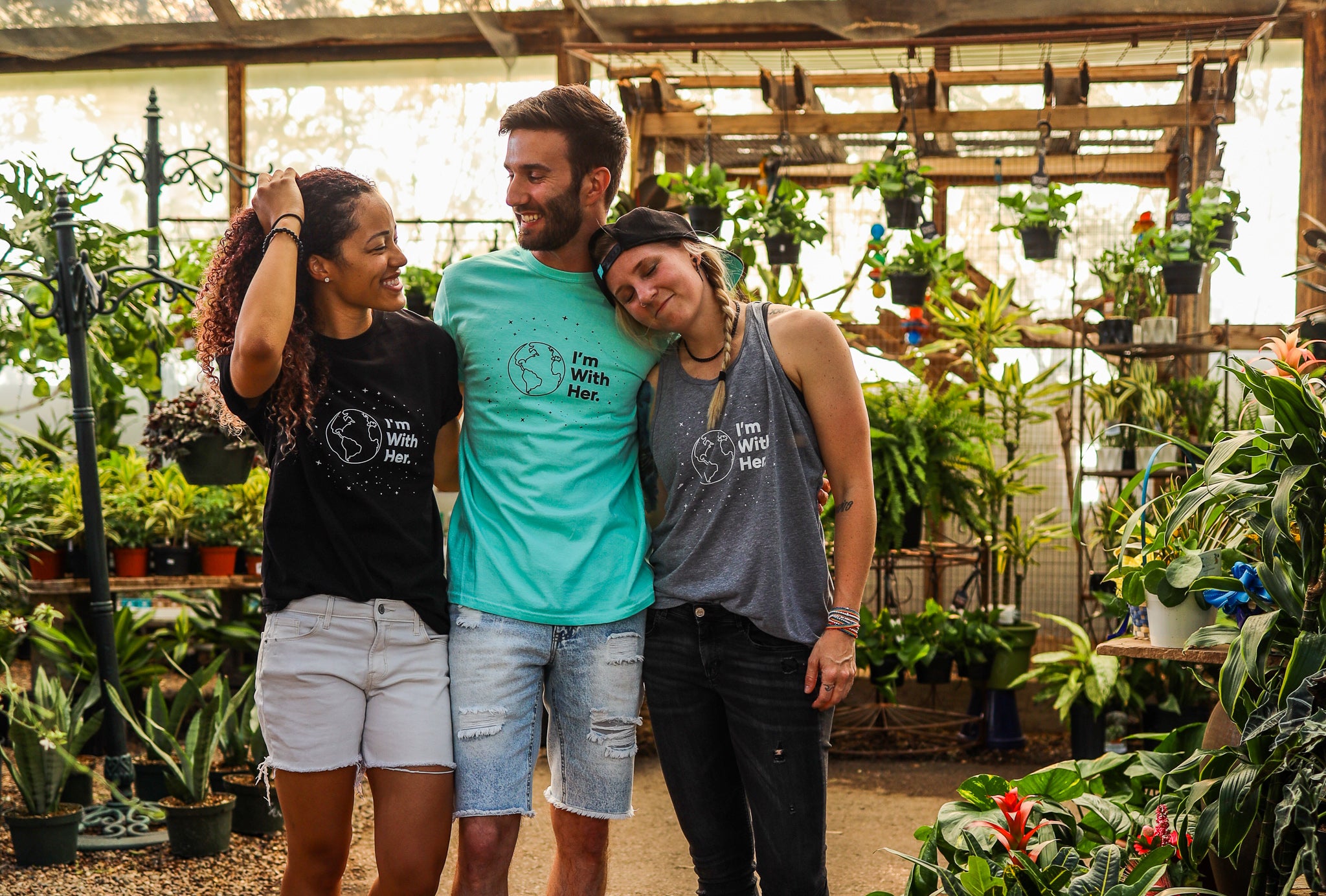 photo of 3 humans wearing only human shirts that read "I'm with her" while in a greenhouse