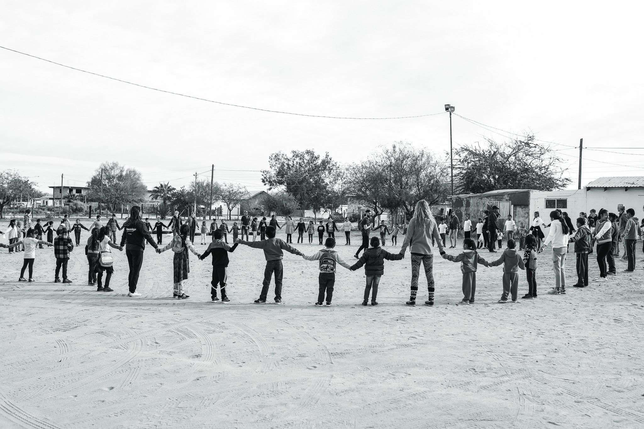 black and white photo of large group of humans holding hands in a chain around a circle