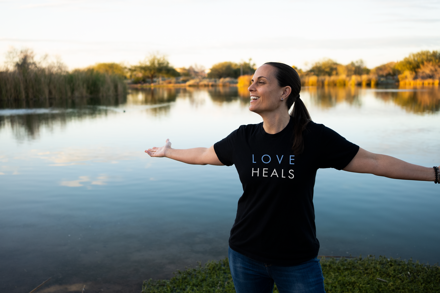 photo of human with arms spread wearing only human shirt that reads "LOVE HEALS"